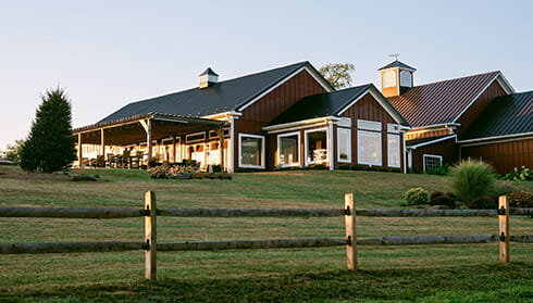 Slater Run Vineyards - Fauquier Wine - view of sunset hitting the upscale barn-like winery front over a wooden fence